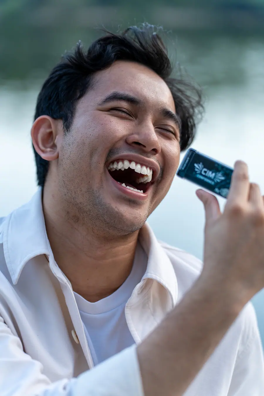 A man laughing openly by the water, holding a CIM mint case