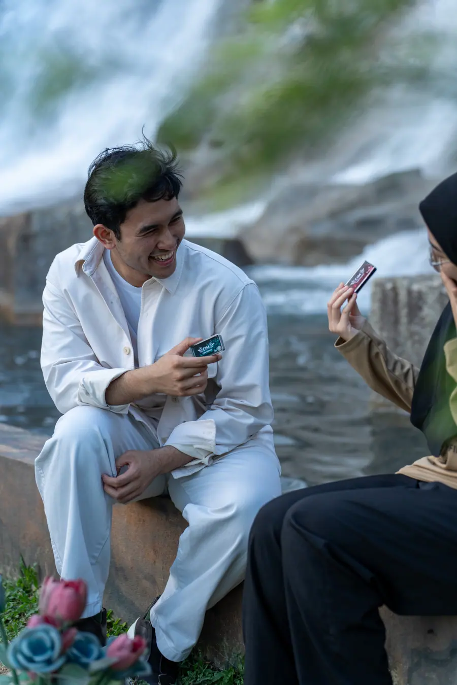 Two friends by a waterfall, each holding a CIM case